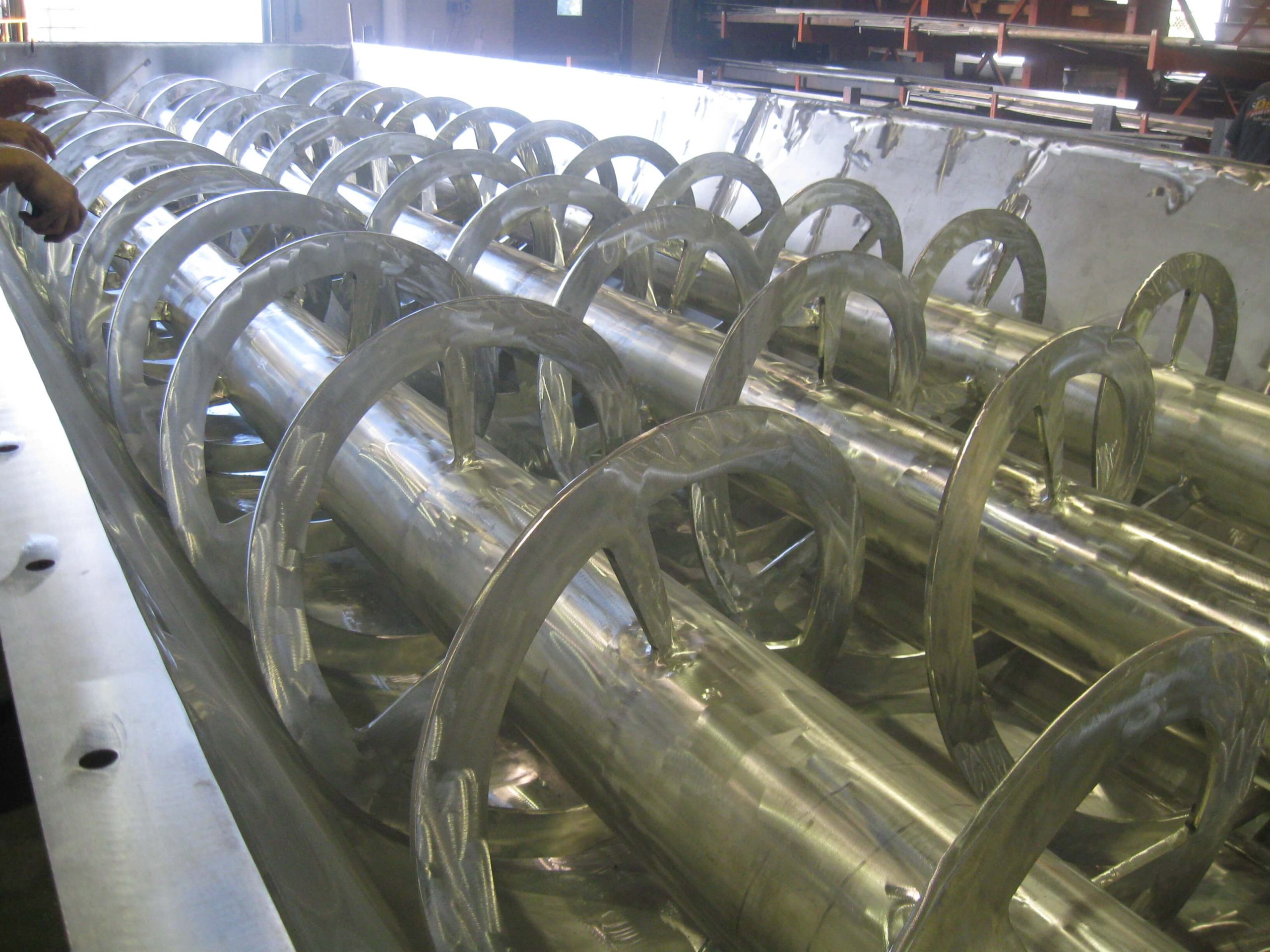 Close-up of ribbon screw flighting inside a stainless steel trough