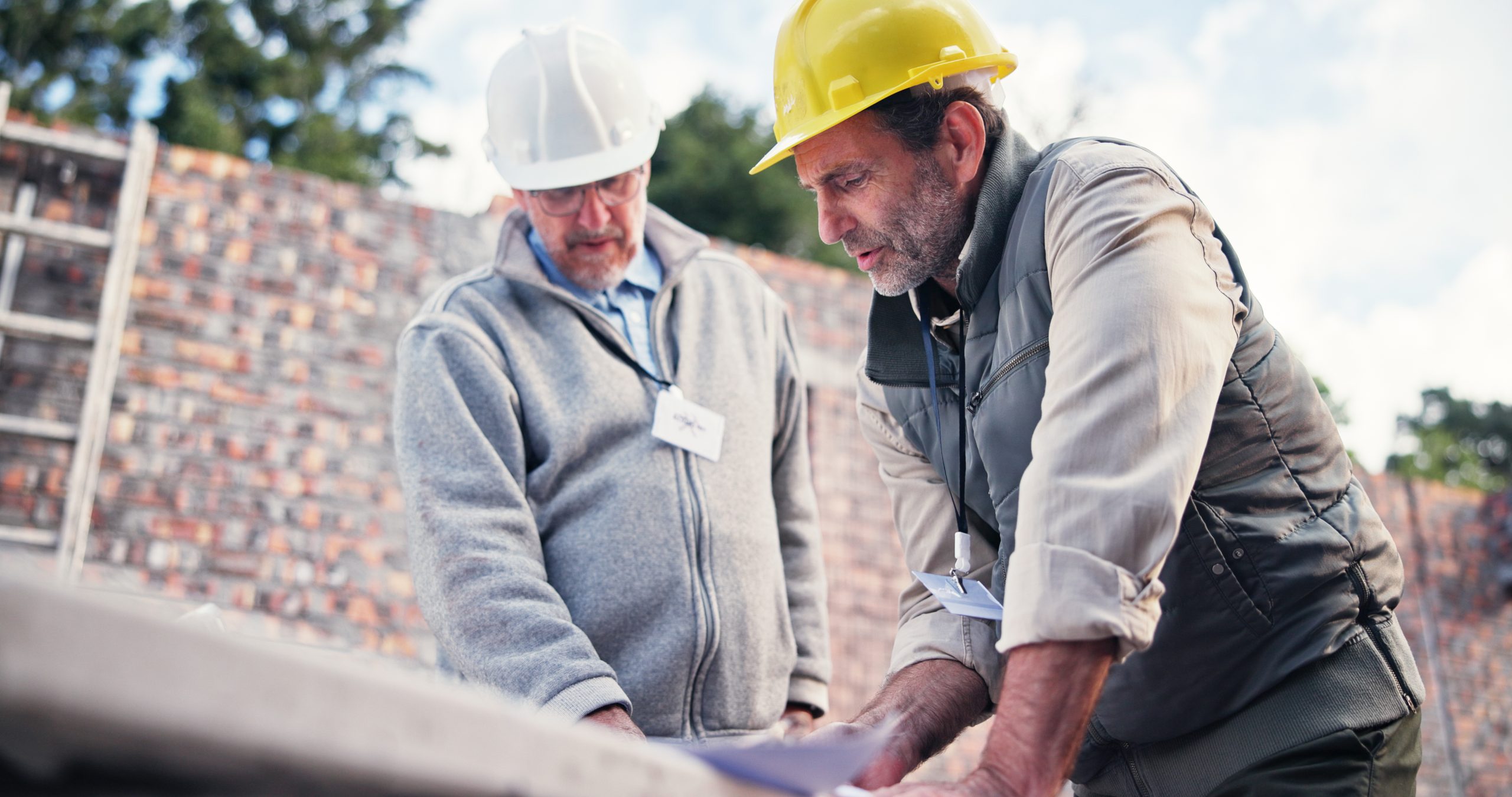 Two engineers in hard hats reviewing plans at a construction site