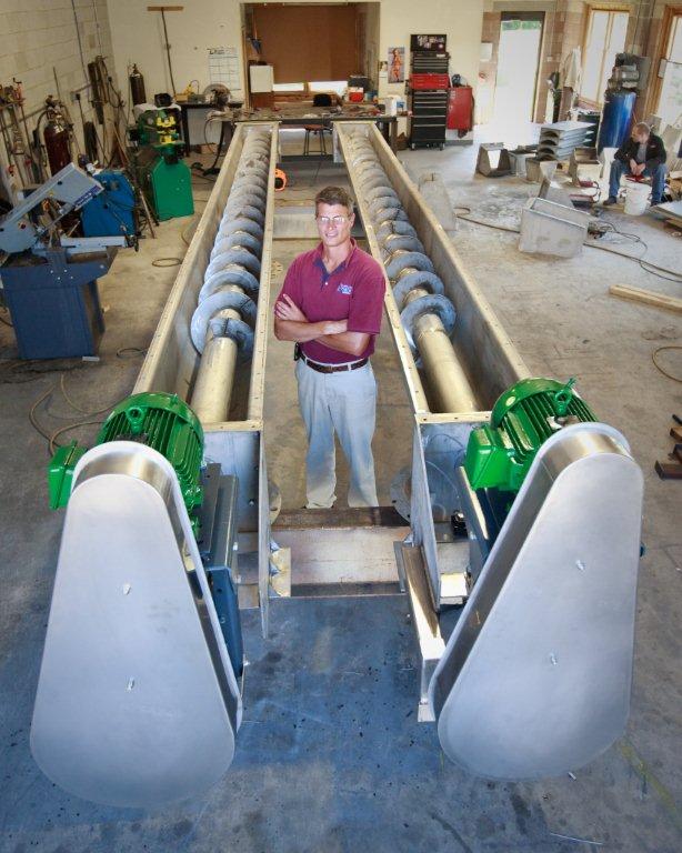 Thomas and Muller employee standing beside large twin screw conveyors